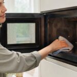 Nettoyage micro-ondes maison Femme nettoyant l'intérieur de son four à micro-ondes avec un chiffon dans une cuisine lumineuse