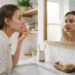 Jeune femme observant sa zone T brillante devant le miroir près d'un savon solide